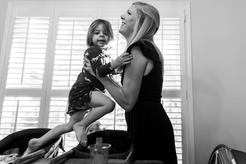 Happy young mom, taking daughter out of high chair during in home photo session. 
