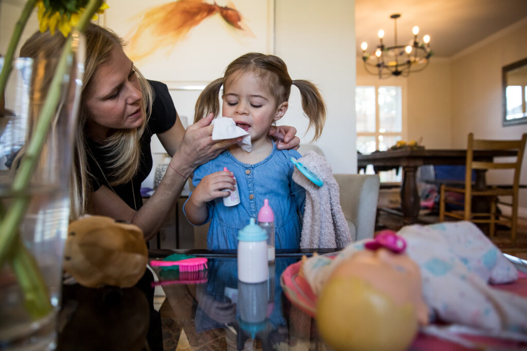 Mom wiping girl toddler's nose with her hair in pigtails during in home session in Denver, Colorado.