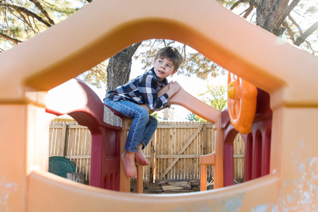 Barefoot boy climbing on colorful play structure in his backyard.