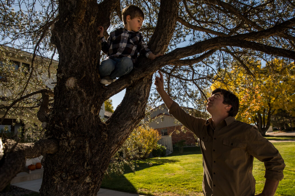 Boy in tree on sunny day in Denver, Colorado with dad looking up and talking to him.