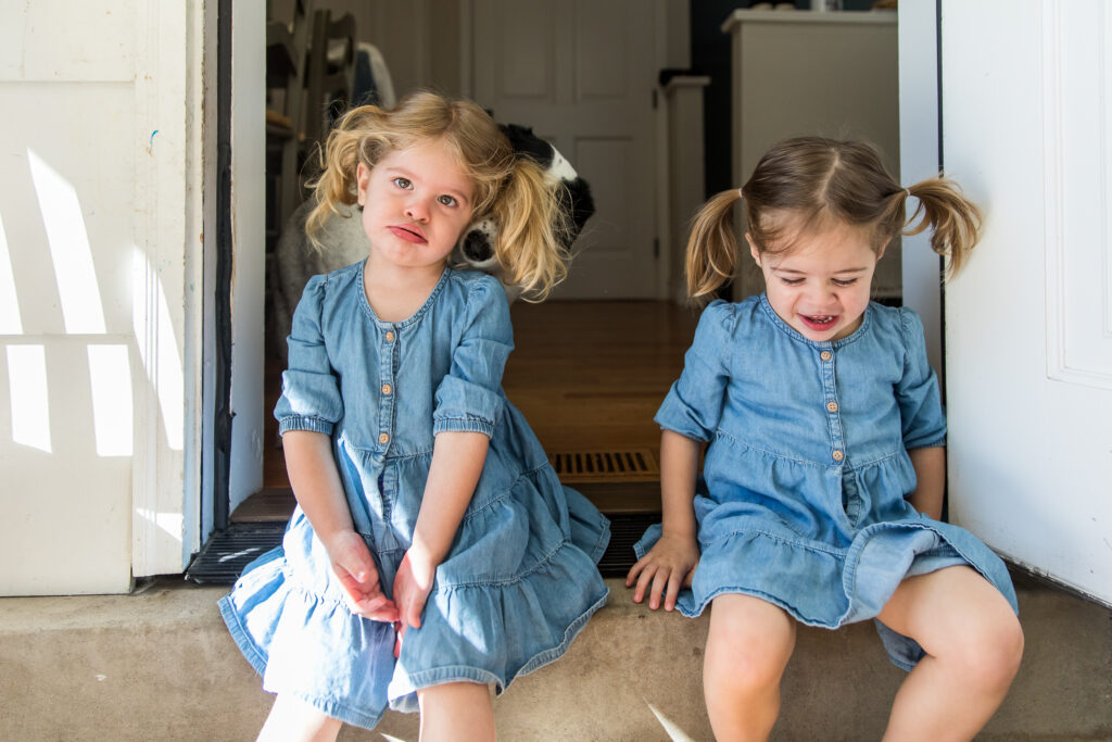 Twins sitting on porch step, dog sniffing girl's ear during in-home session in Denver, Colorado.