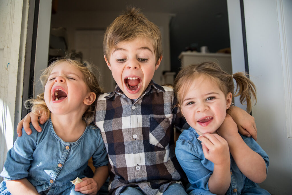 Three siblings giggling while sitting in their doorway during an in home session.