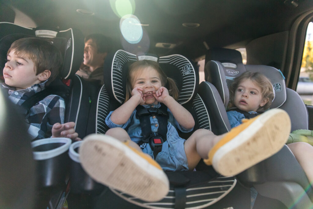 Three siblings, giggling and sitting in their carseats on their way to a park in Denver, Colorado.
