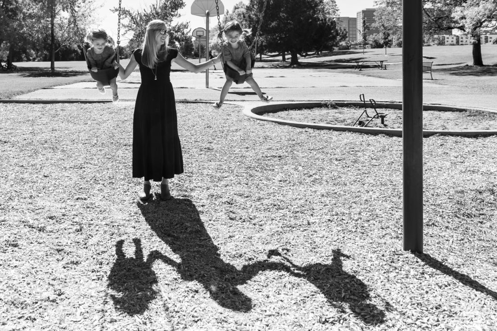 Mom pushing smiling twin girls on a swing in Denver Colorado.