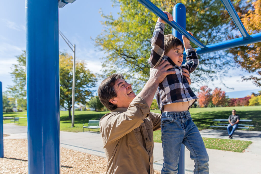 Dad helping son across monkey bars at a park.