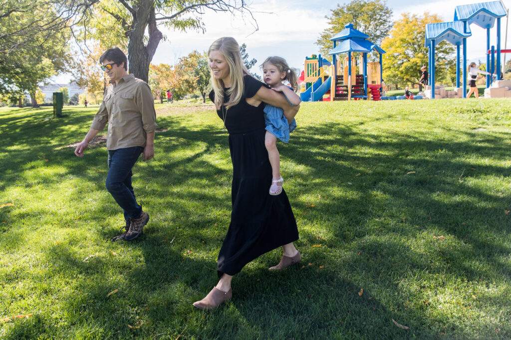 Mom and dad walking with toddler on a sunny day at a Denver CO park during a day in the life photo session.