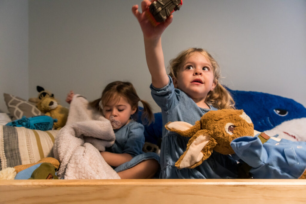 Twins snuggling with stuffies and blankets on top bunk during in home session in Denver, Colorado.